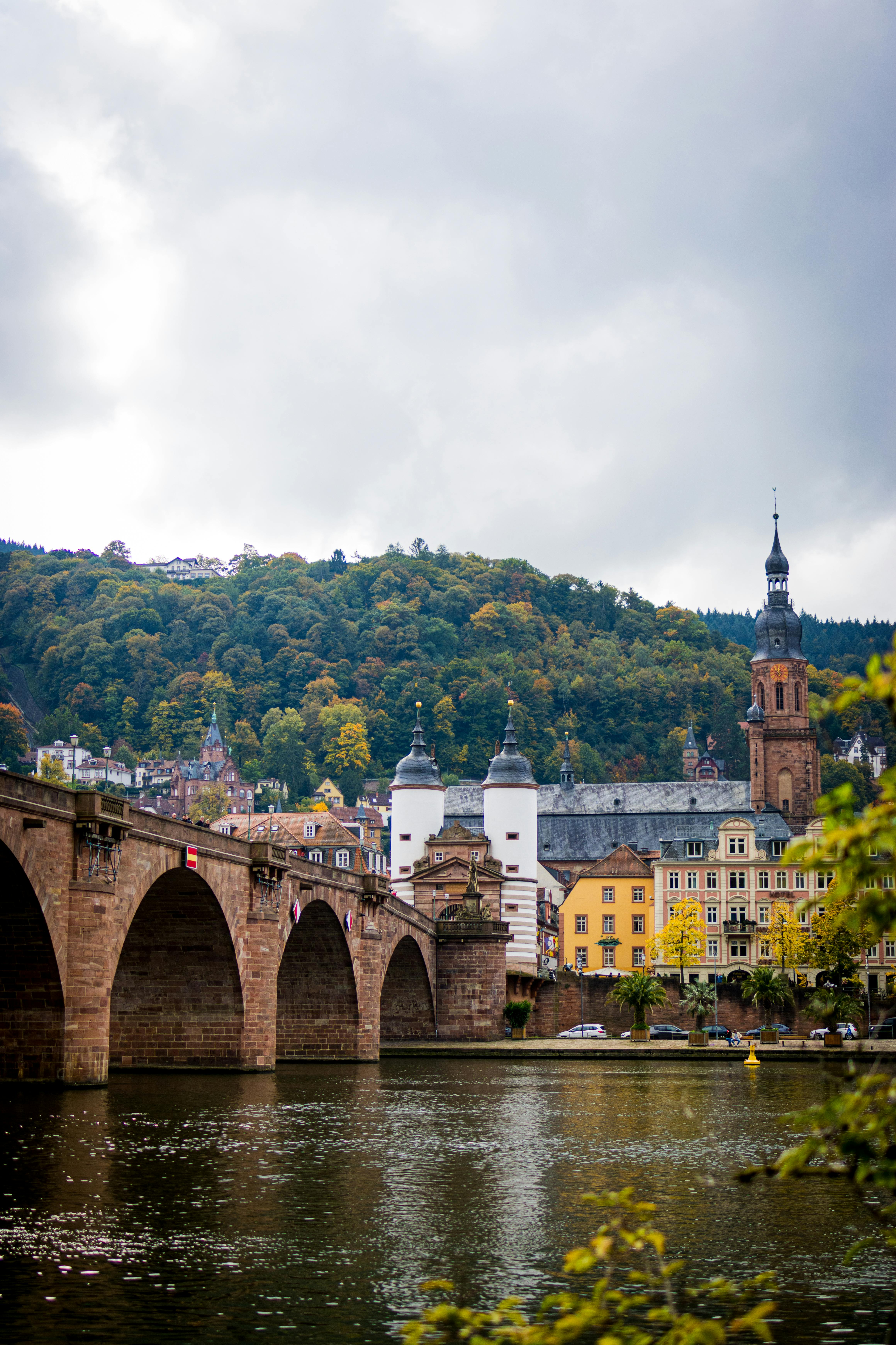 Scenic view of Heidelberg's historic bridge over a calm river with autumn foliage.