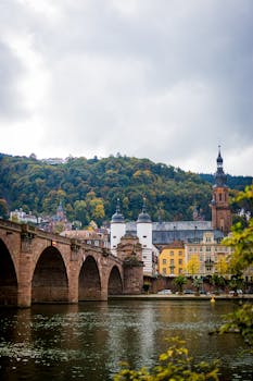 Scenic view of Heidelberg's historic bridge over a calm river with autumn foliage.