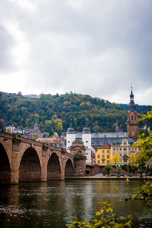 Free Scenic view of Heidelberg's historic bridge over a calm river with autumn foliage. Stock Photo