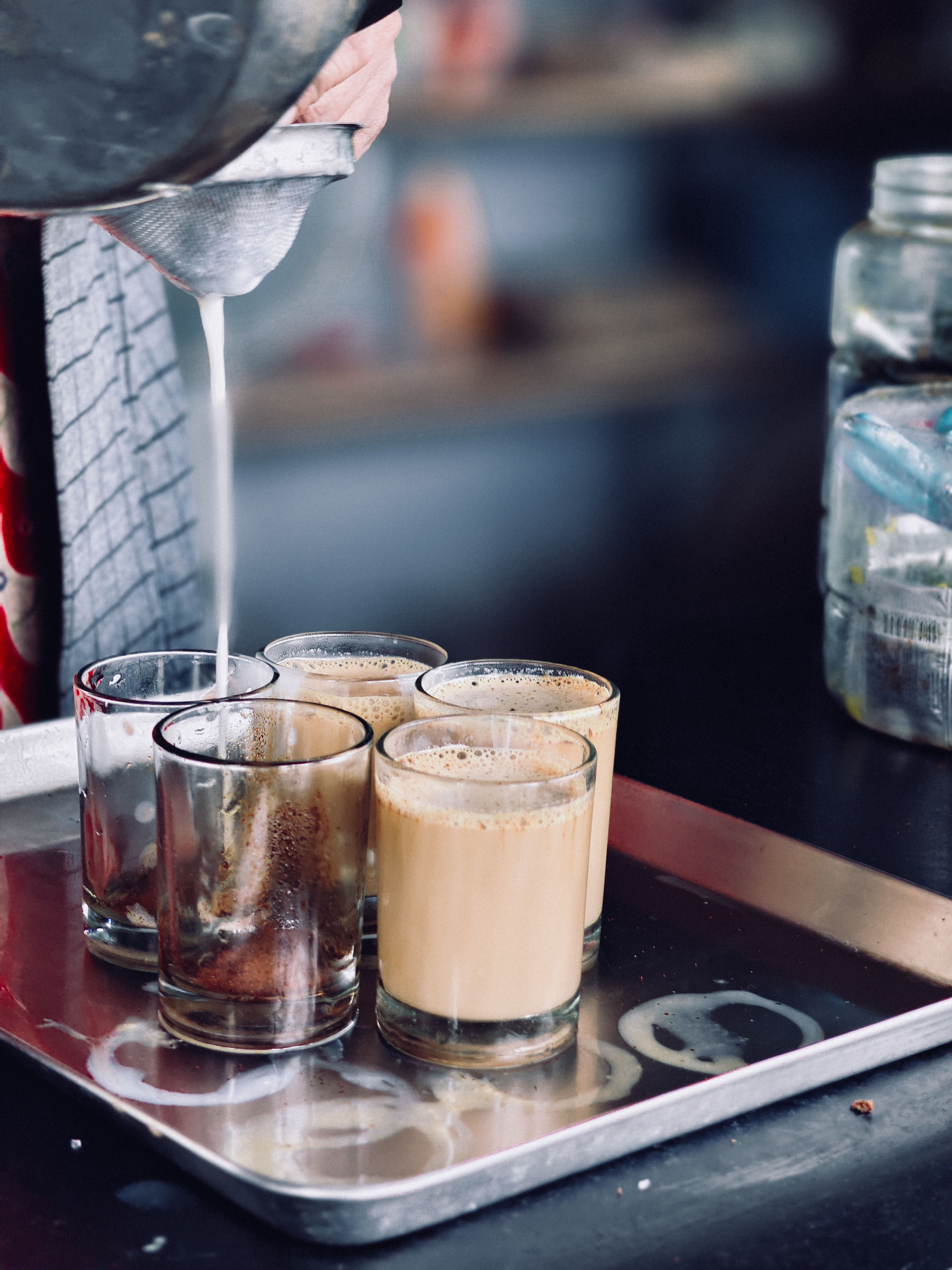 Close-up of street vendor pouring chai into small glasses, creating a lively street food scene.