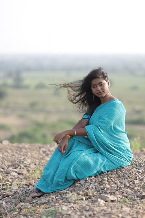 Free Portrait of a woman in a blue saree sitting outdoors, exuding calmness. Stock Photo