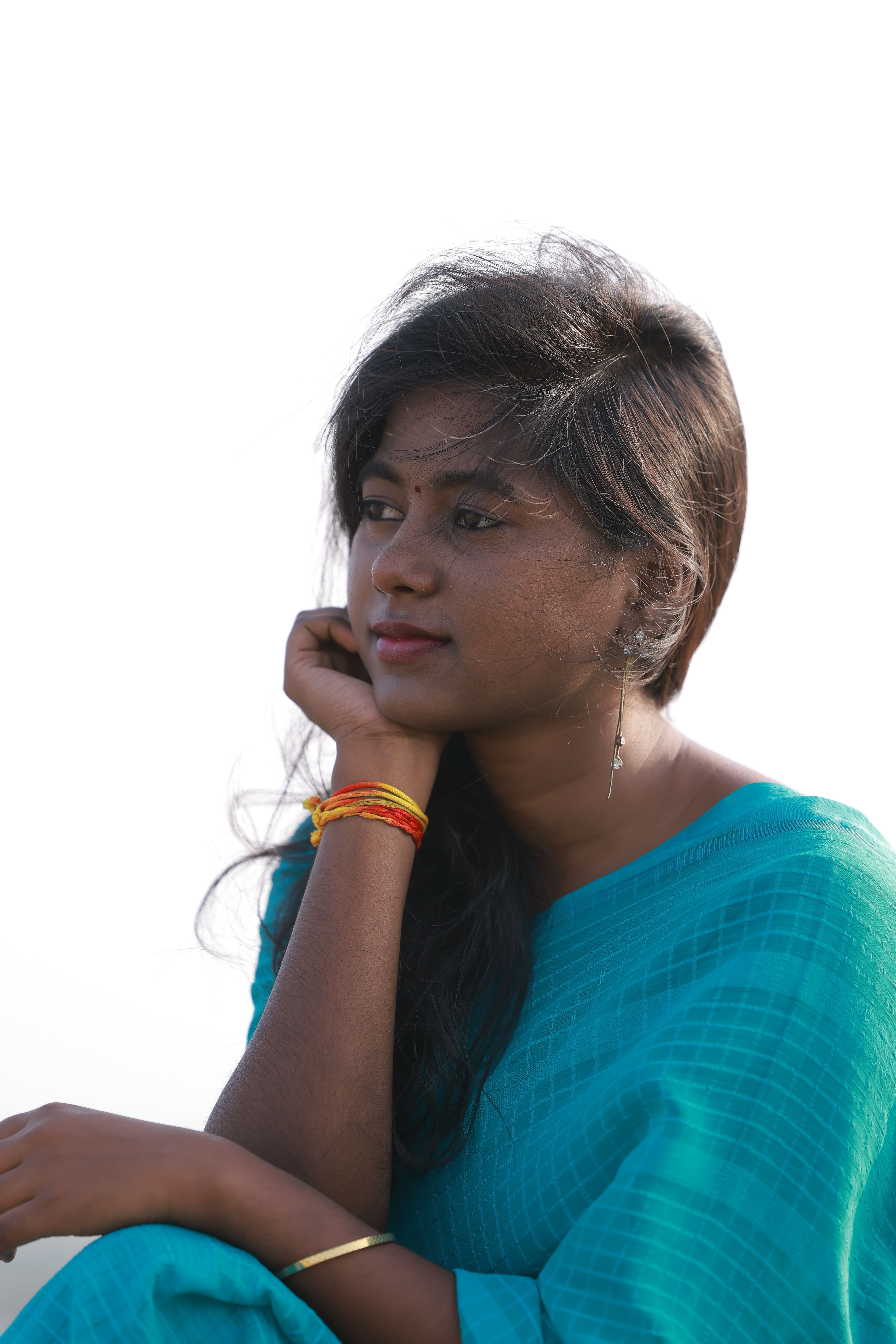 A young woman in a turquoise saree gazing thoughtfully outdoors on a clear day.