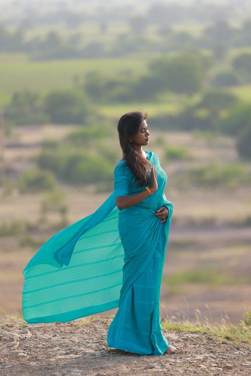 Free A woman in a blue saree stands gracefully on a hill, enjoying a peaceful outdoor view. Stock Photo