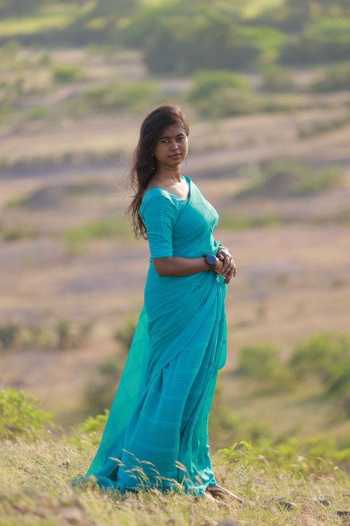 Free A serene portrait of a woman in a turquoise sari standing in a natural landscape. Stock Photo