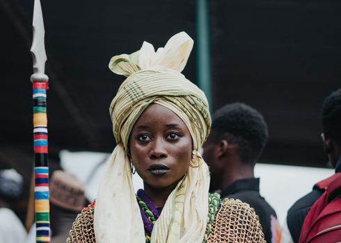 Woman wearing traditional African attire with a spear at a cultural festival, showcasing heritage and style.