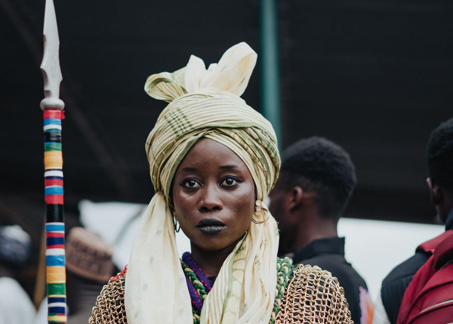 Woman wearing traditional African attire with a spear at a cultural festival, showcasing heritage and style.