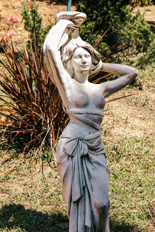 Free Graceful stone statue of a woman in an outdoor garden with vibrant greenery. Stock Photo