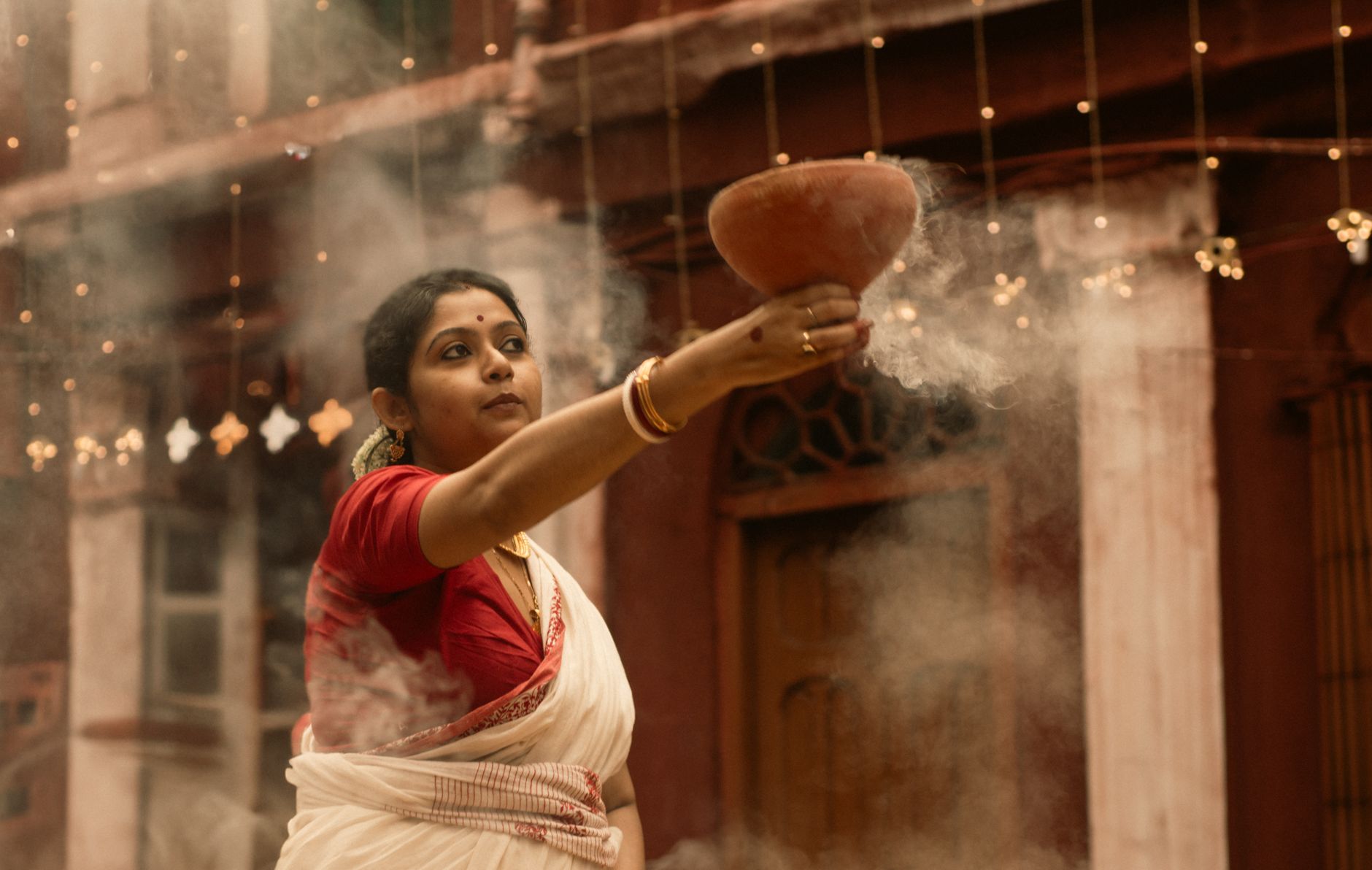 A woman in traditional attire performs a ritual with incense in a cultural setting.