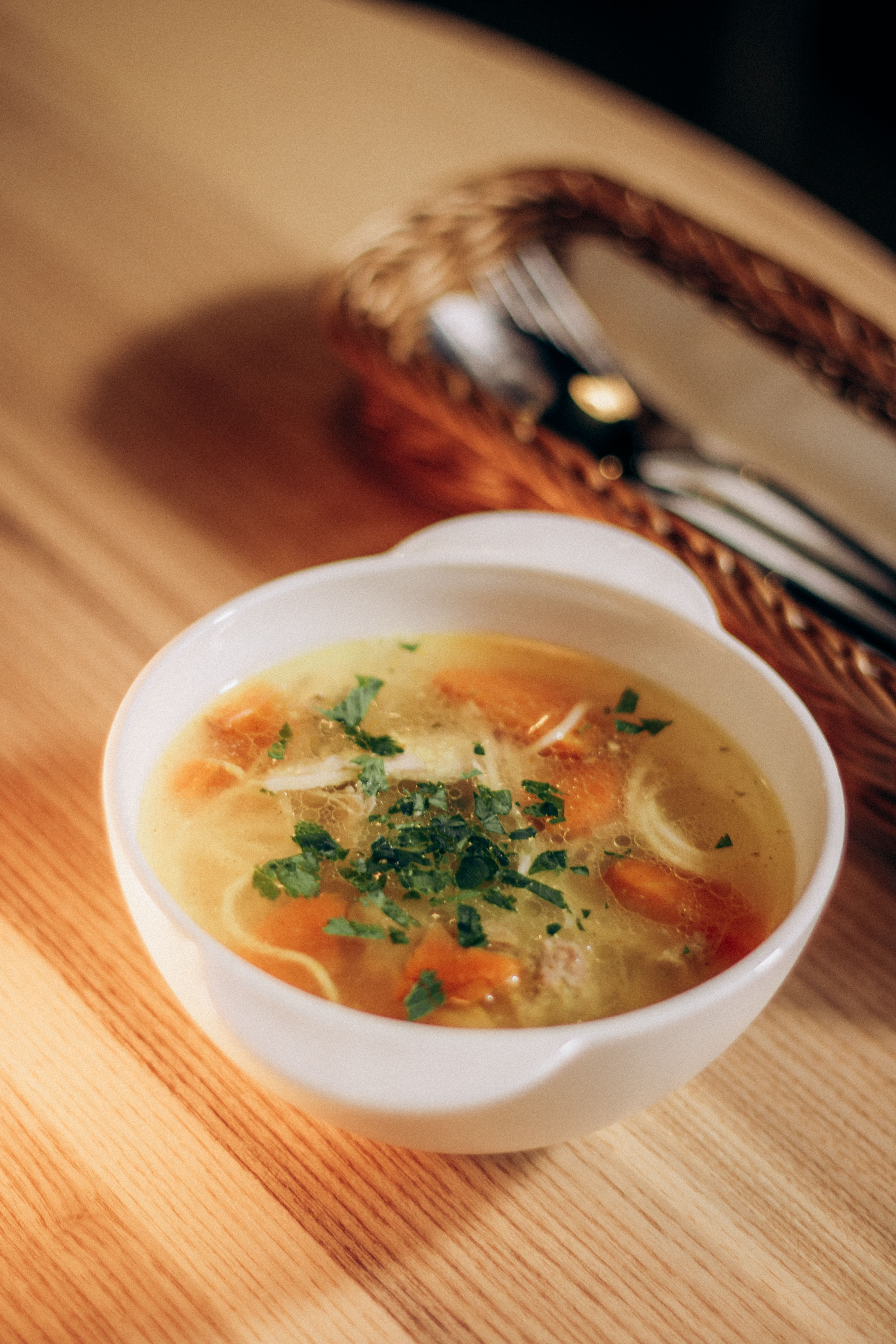 Close-up of delicious chicken soup with carrots and herbs in a white bowl, perfect for cozy meals.