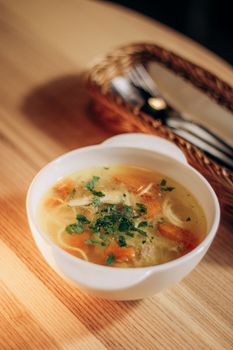 Close-up of delicious chicken soup with carrots and herbs in a white bowl, perfect for cozy meals.