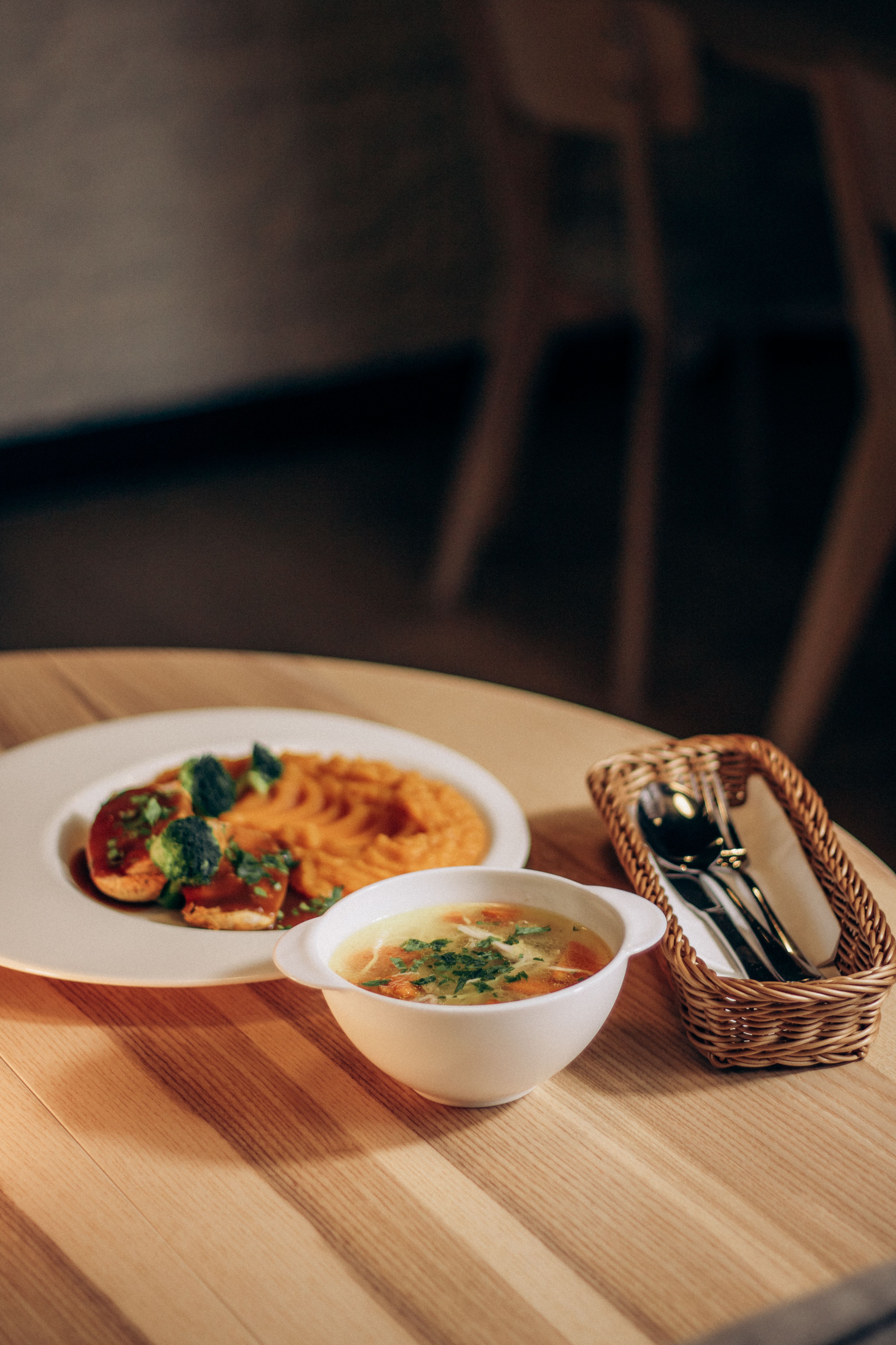 A beautifully plated vegetarian meal featuring soup and pasta on a wooden table setting.
