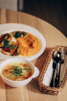Delicious chicken soup with vegetables and a side of mashed potatoes on a wooden table.