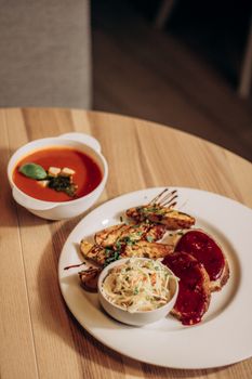 Savory dish with grilled potatoes, meatloaf, cole slaw, and tomato soup on a wooden table.