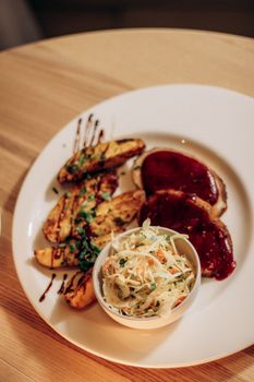 Plated gourmet meal with grilled potatoes, meat with sauce, and a side of slaw, perfect for food photography.