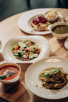 A selection of Mediterranean dishes including salad, pasta, and soup served on a wooden table.
