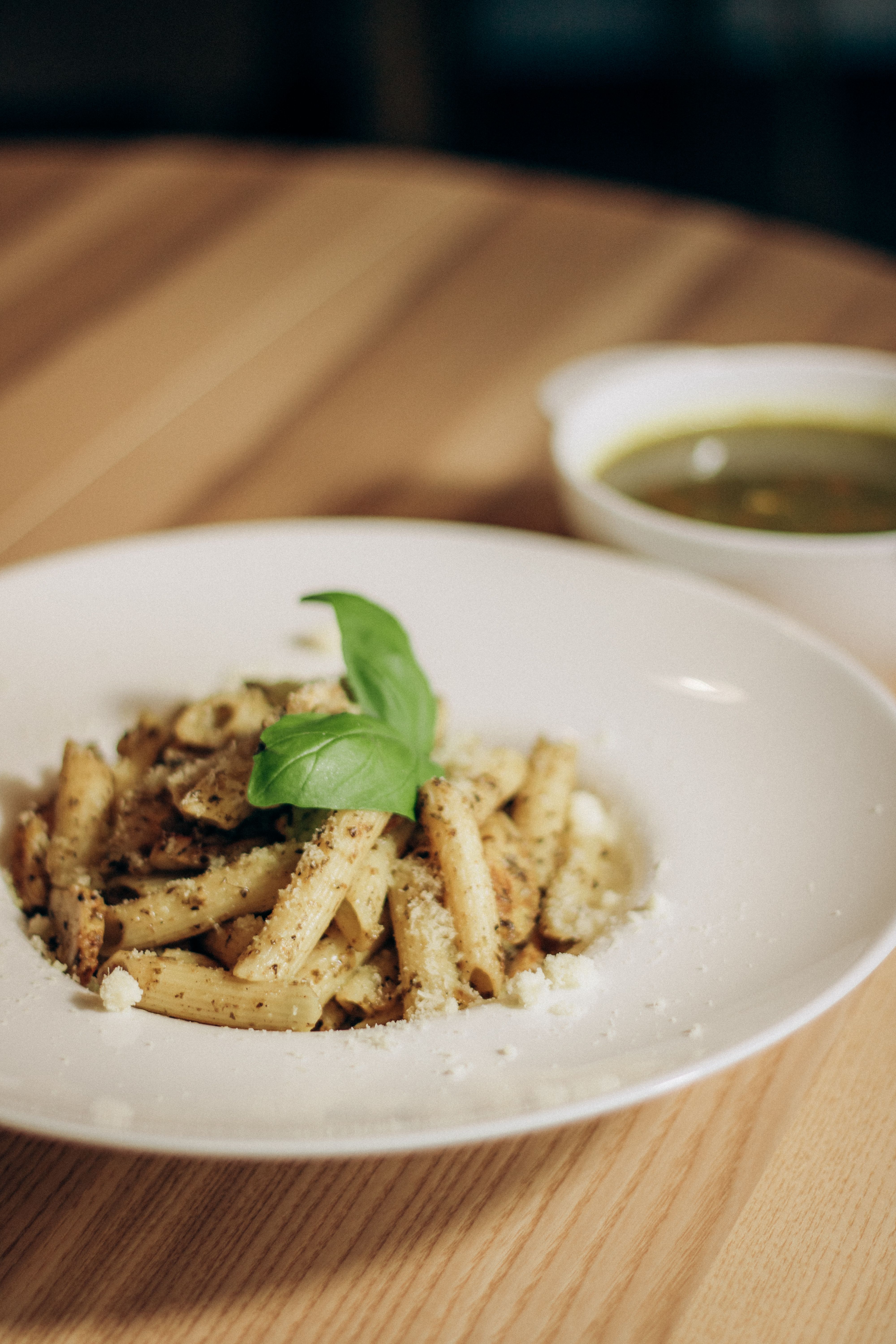Freshly cooked pesto pasta with parmesan and basil on a wooden table, offering a homestyle dining feel.