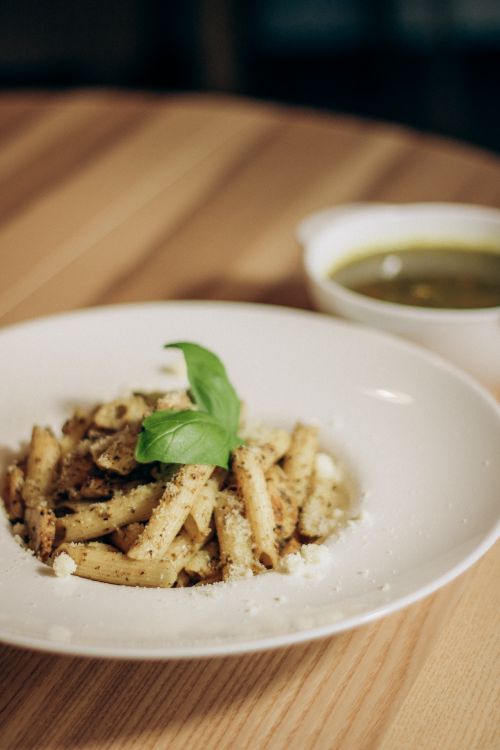 Free Close-up of herb-crusted pasta garnished with basil, served on a wooden table. Stock Photo