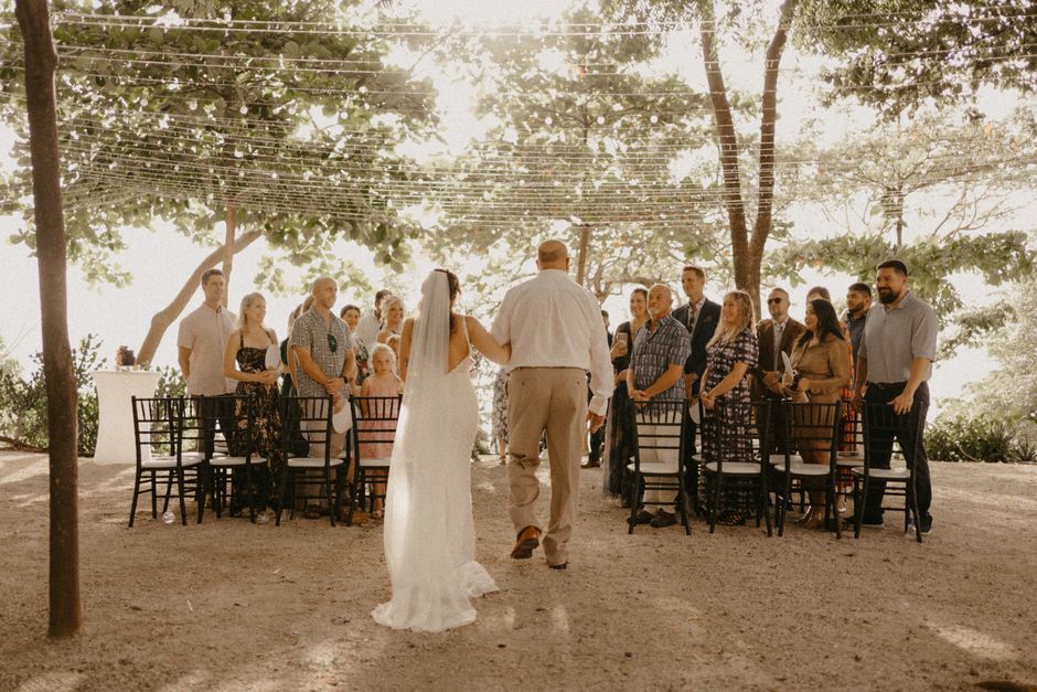 Bride walking down the aisle outdoors with a groom under string lights.