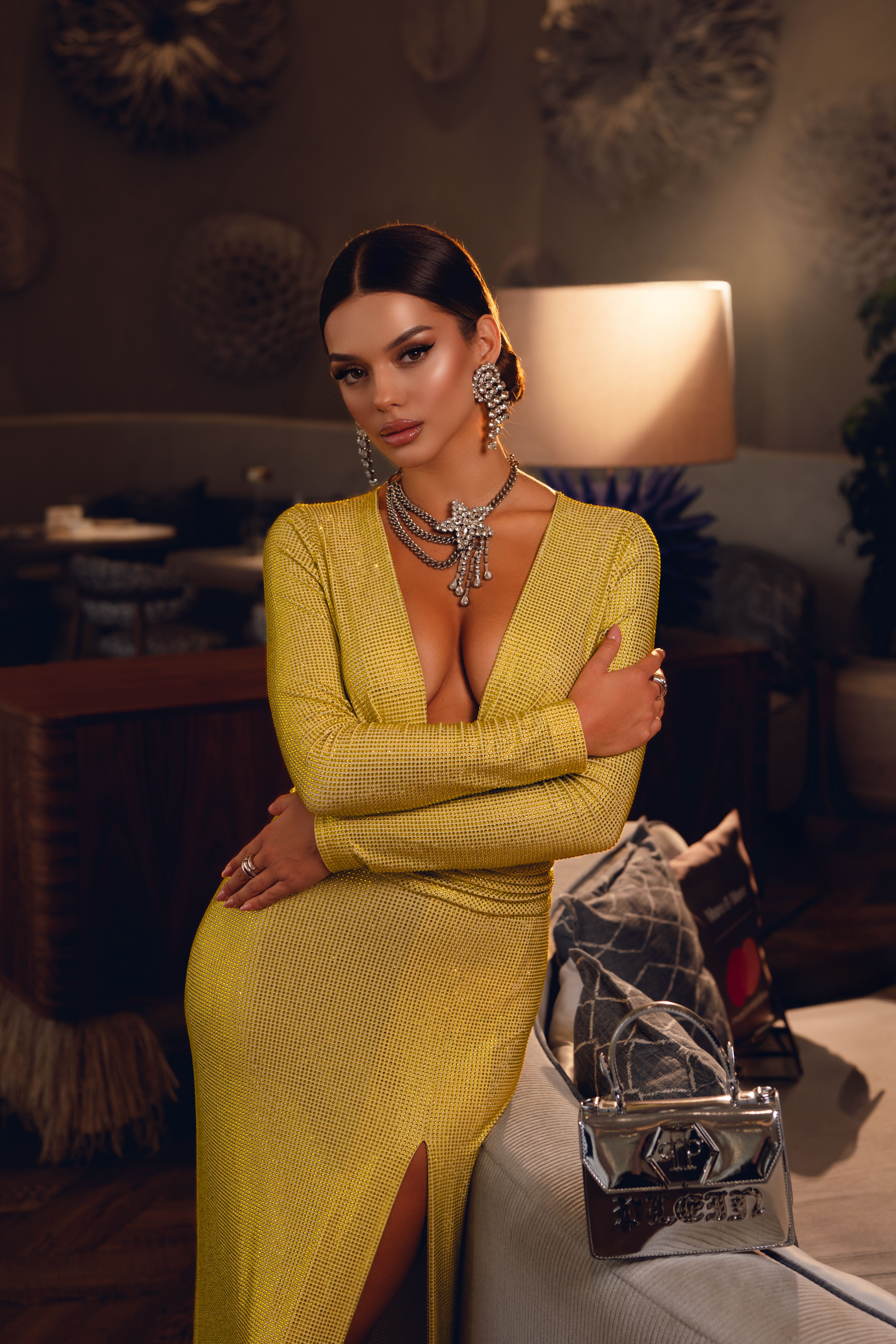 Graceful woman in luxurious yellow gown posing indoors at night with elegant jewelry.