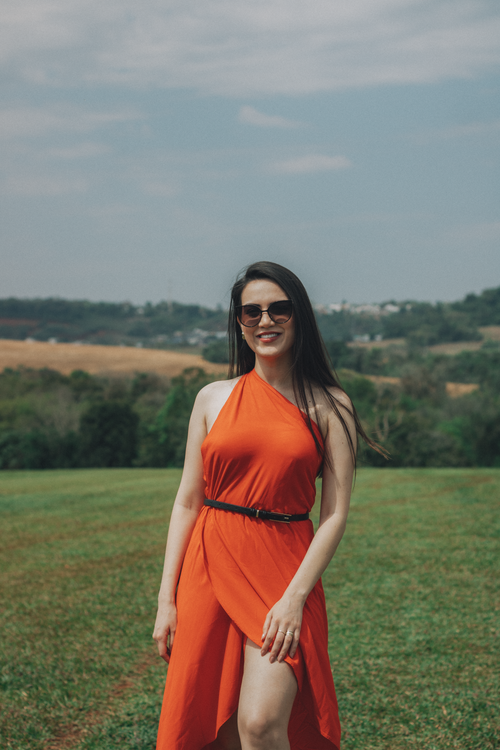 Free Confident woman in a red dress and sunglasses standing on a sunny hillside. Stock Photo