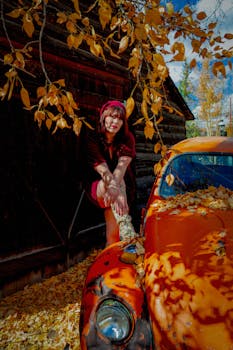 Fashionable woman posing with Volkswagen Beetle surrounded by vibrant fall foliage.