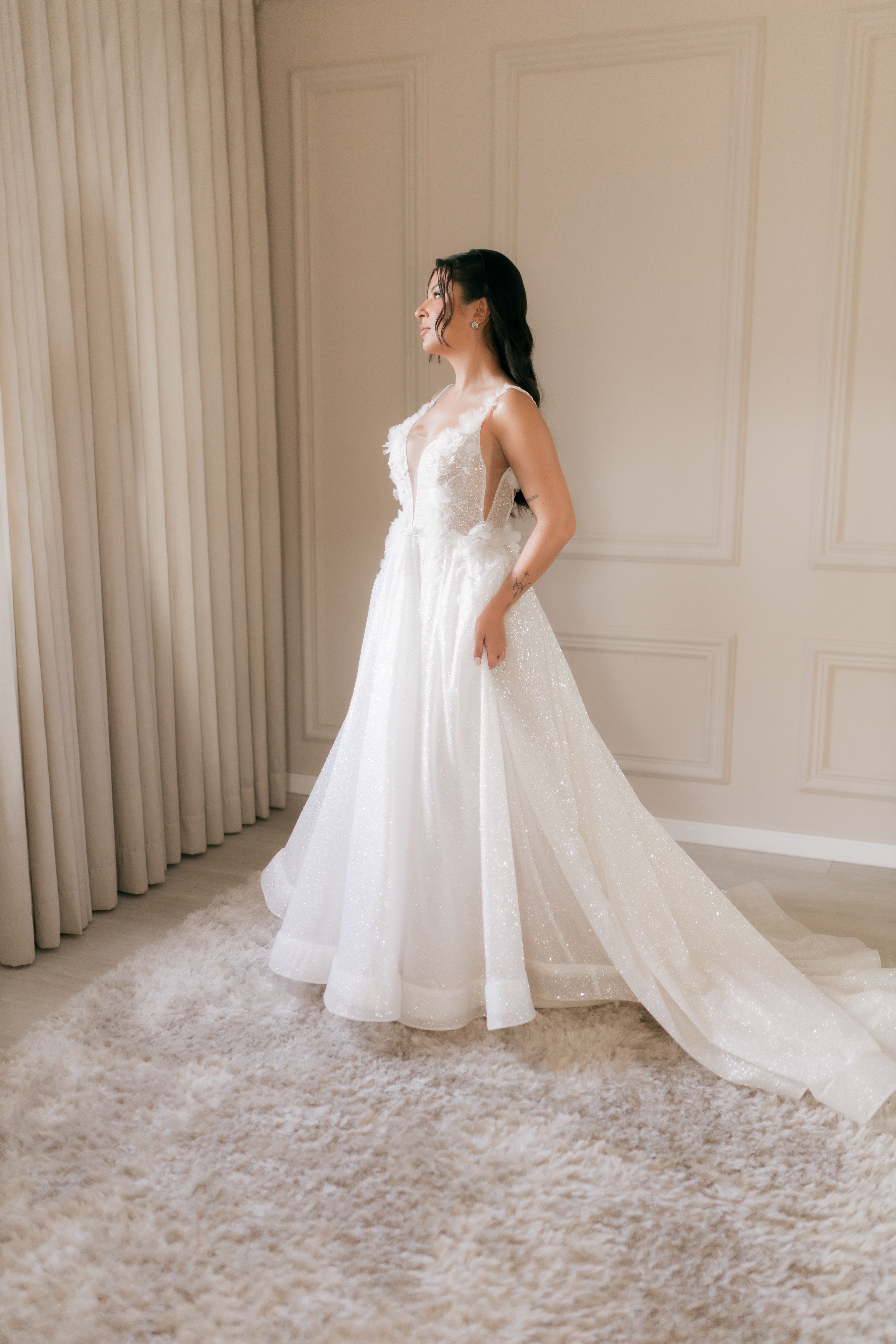 Bride posing in an elegant white wedding gown by a window, exuding grace and beauty.