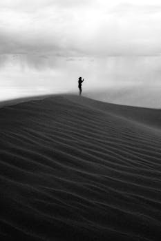 A solitary person stands on a sand dune in Algeria, surrounded by a dramatic landscape.
