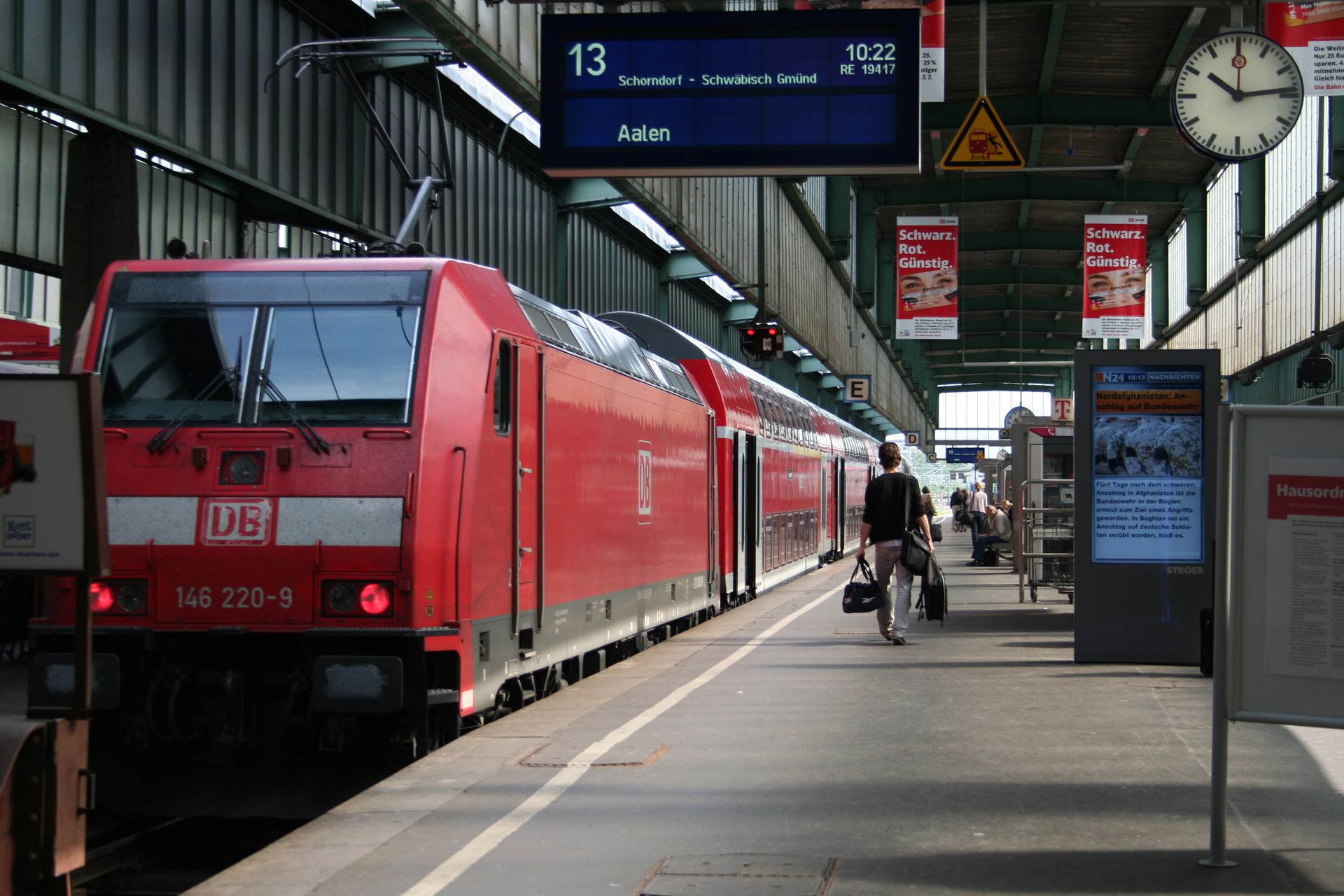 A red DB train at Aalen station platform with passengers preparing to board.