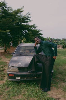 Portrait of a man casually resting on an old car in a rural Nigerian setting.