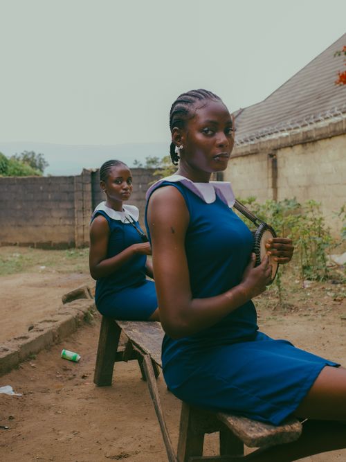 Two Nigerian schoolgirls in blue uniforms sitting outdoors