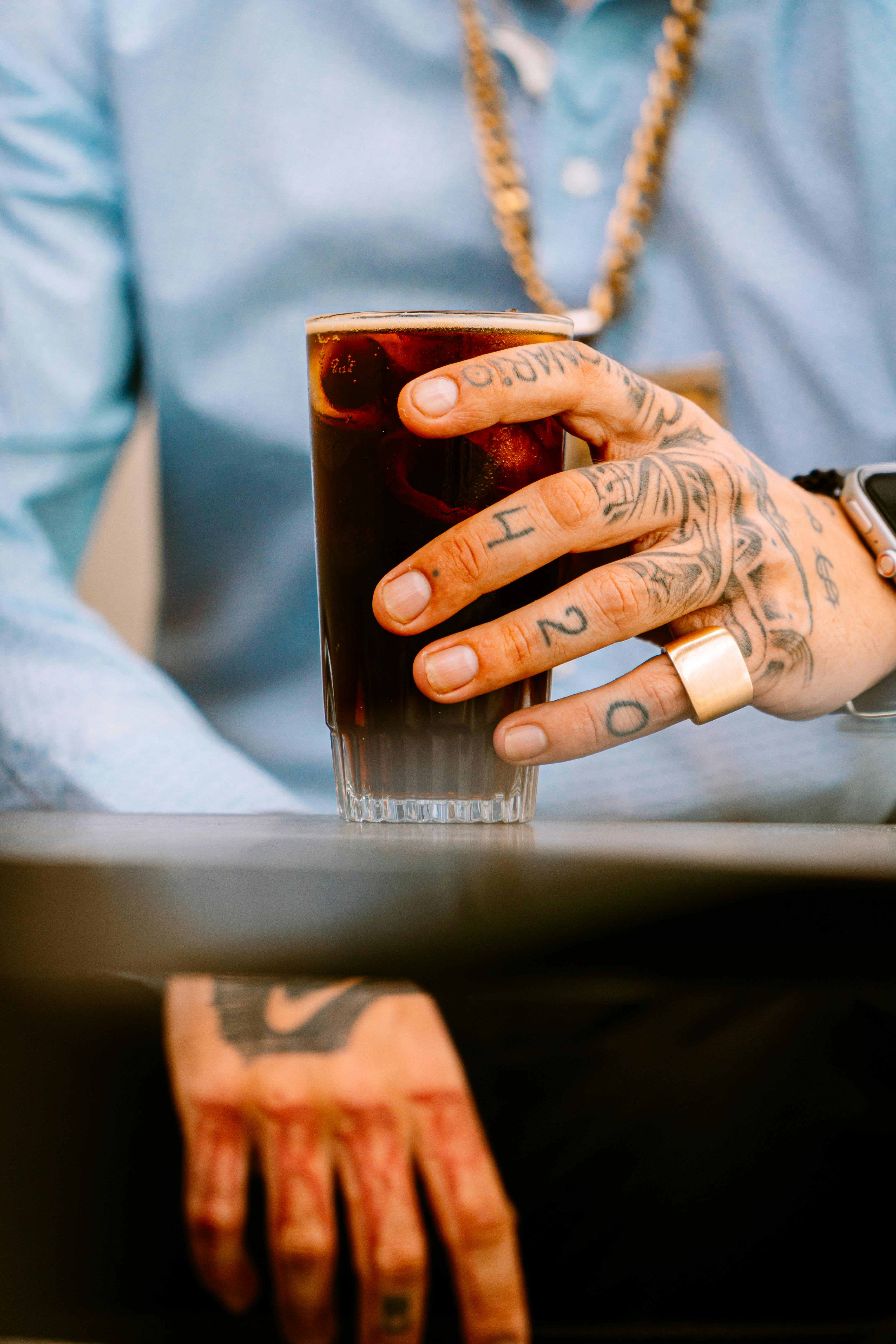 De franc Mà tatuada que sosté un got de beguda negra en un bar de Buenos Aires, Argentina. Foto d'estoc