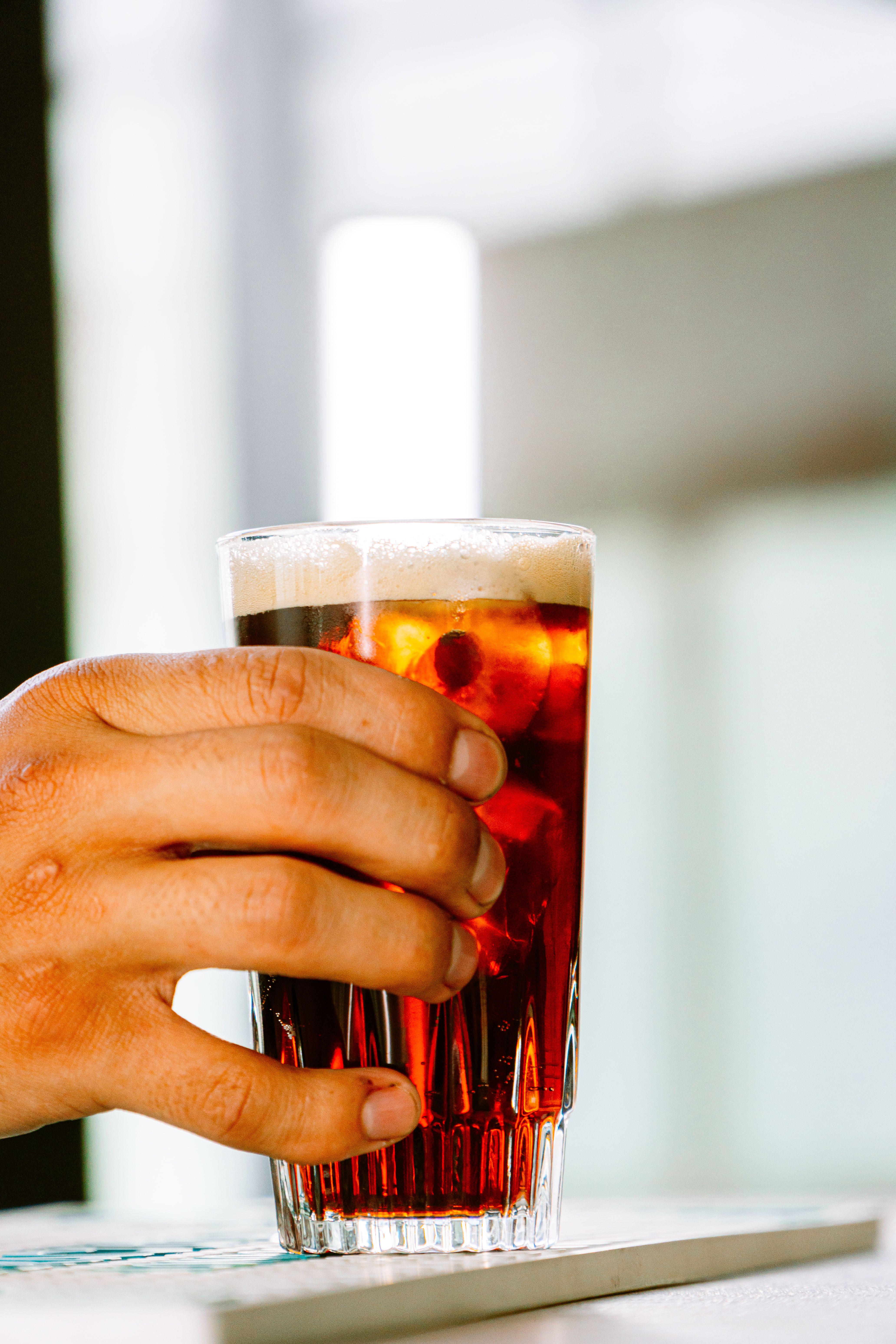 Close-up of a hand holding a glass of fernet with ice in a modern bar in Buenos Aires.