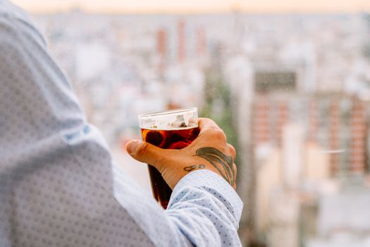 A person holding a glass of Fernet overlooking Buenos Aires cityscape.