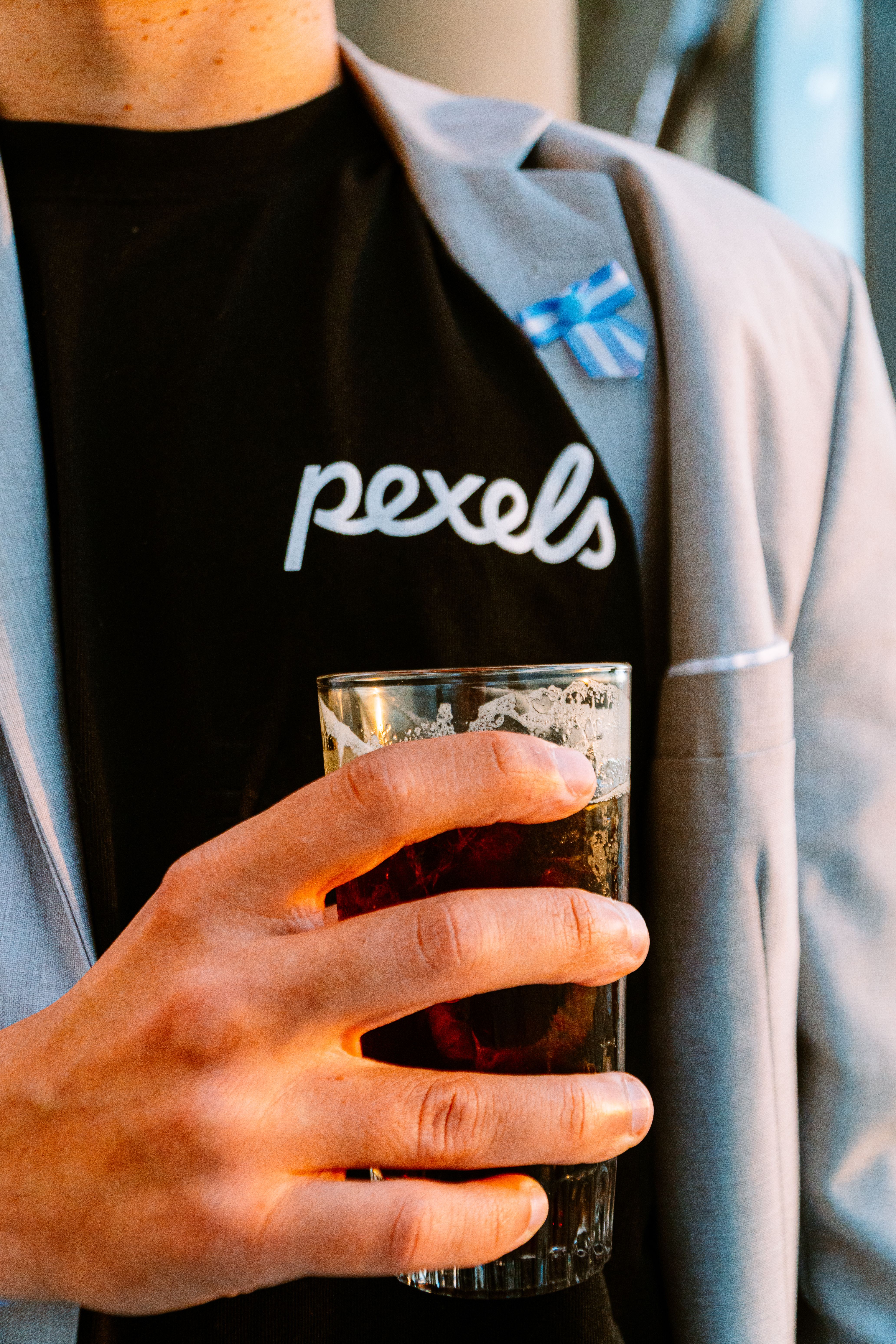 Person in a suit holding a drink with an Argentinian flag pin on lapel. Stylish and modern ambiance.