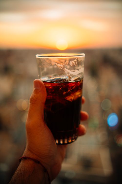Free Hand holding a glass of Fernet with ice against a vibrant sunset in Buenos Aires, Argentina. Stock Photo