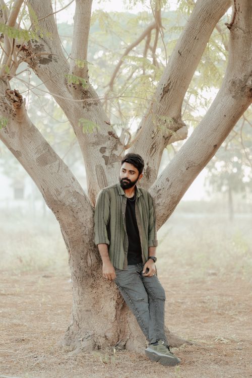 Free Young man with beard leaning against a tree in a serene outdoor setting. Stock Photo