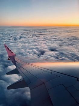 View from an airplane wing overlooking clouds at sunset, showcasing serene sky and horizon.