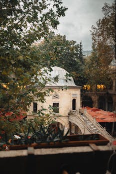 Scenic view of a historic courtyard with a domed building surrounded by lush trees and red umbrellas.
