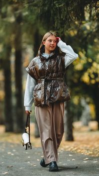 Teen girl strolling in autumn park, wearing trendy shiny vest. Stylish and casual mode in a natural outdoor setting.