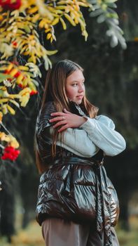 Young girl in a puffer jacket enjoys a serene autumn walk surrounded by colorful leaves.