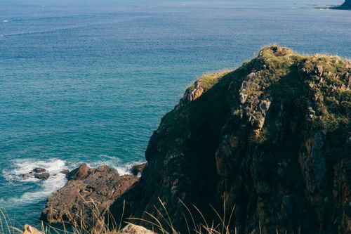 Free Majestic rocky cliff with lush grass overlooking a serene blue ocean under clear skies. Stock Photo