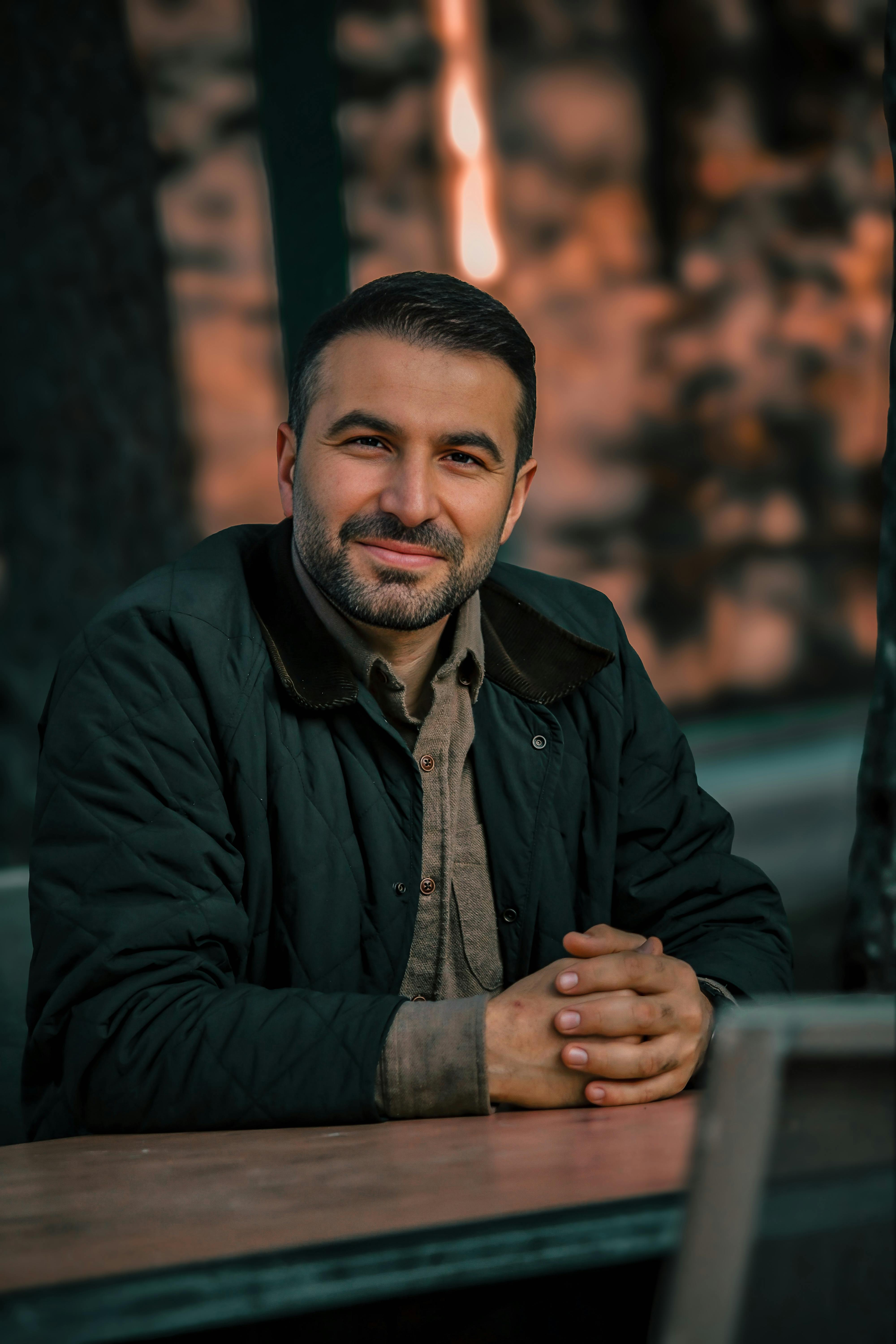 Casual portrait of a man smiling warmly while seated outdoors with a blurred background.