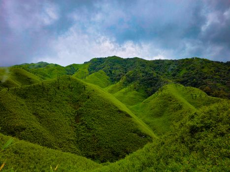 Stunning view of vibrant green hills under a dramatic cloudy sky, located in India.