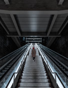 A person in a red hat ascending a modern underground staircase in a Bilbao metro station.
