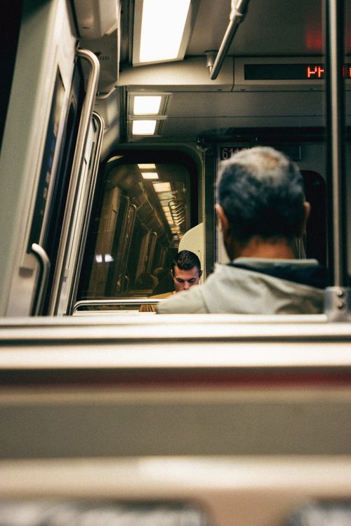 Free Two men seated on a metro train, captured from behind, conveys an urban commute scene. Stock Photo