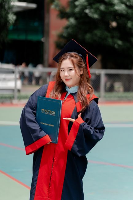Smiling graduate in cap and gown holding diploma outdoors.