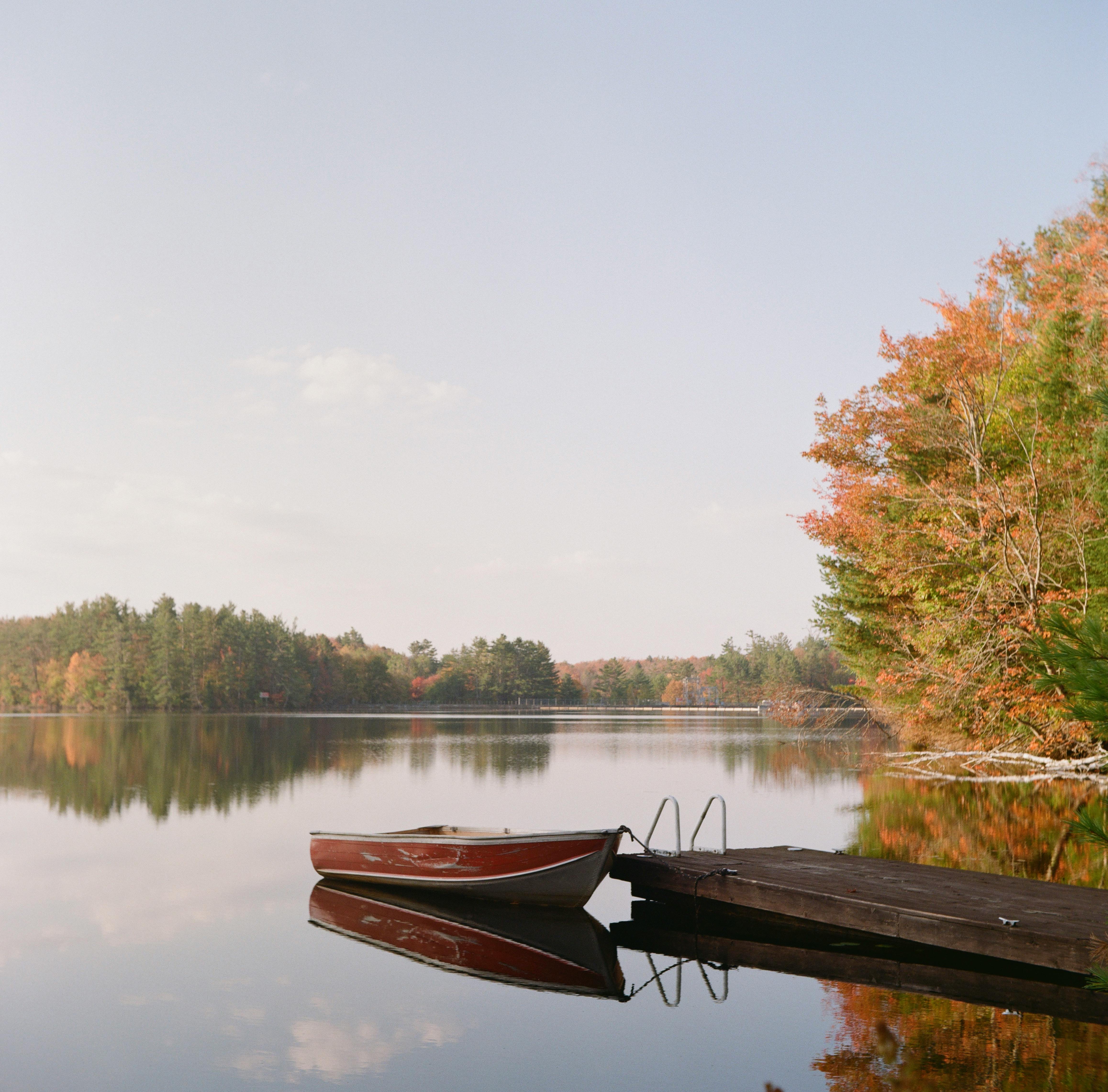 Peaceful autumn lake scene with a boat and dock at sunrise, featuring fall foliage.