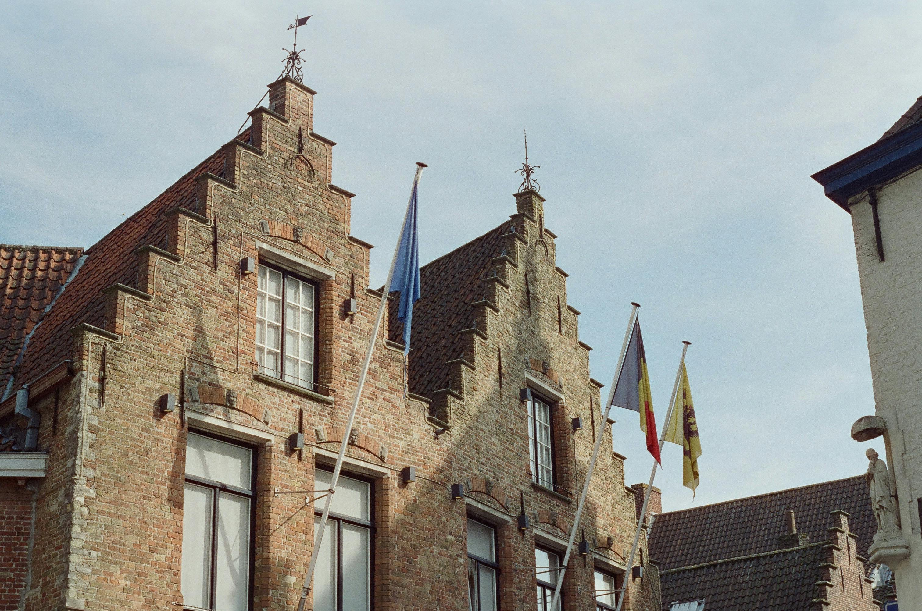 Belçika'nın tarihi bir meydanında yerel kültürü ve günlük yaşamı yansıtan, geleneksel mimari eşliğinde sosyalleşen insanlar ve yerel detaylar.