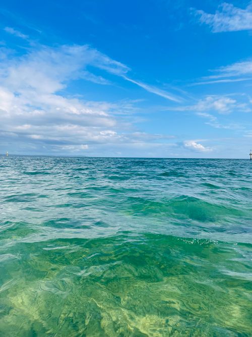 Free Vivid green ocean waters meeting the blue sky with clouds on a sunny day, perfect for travel and nature themes. Stock Photo
