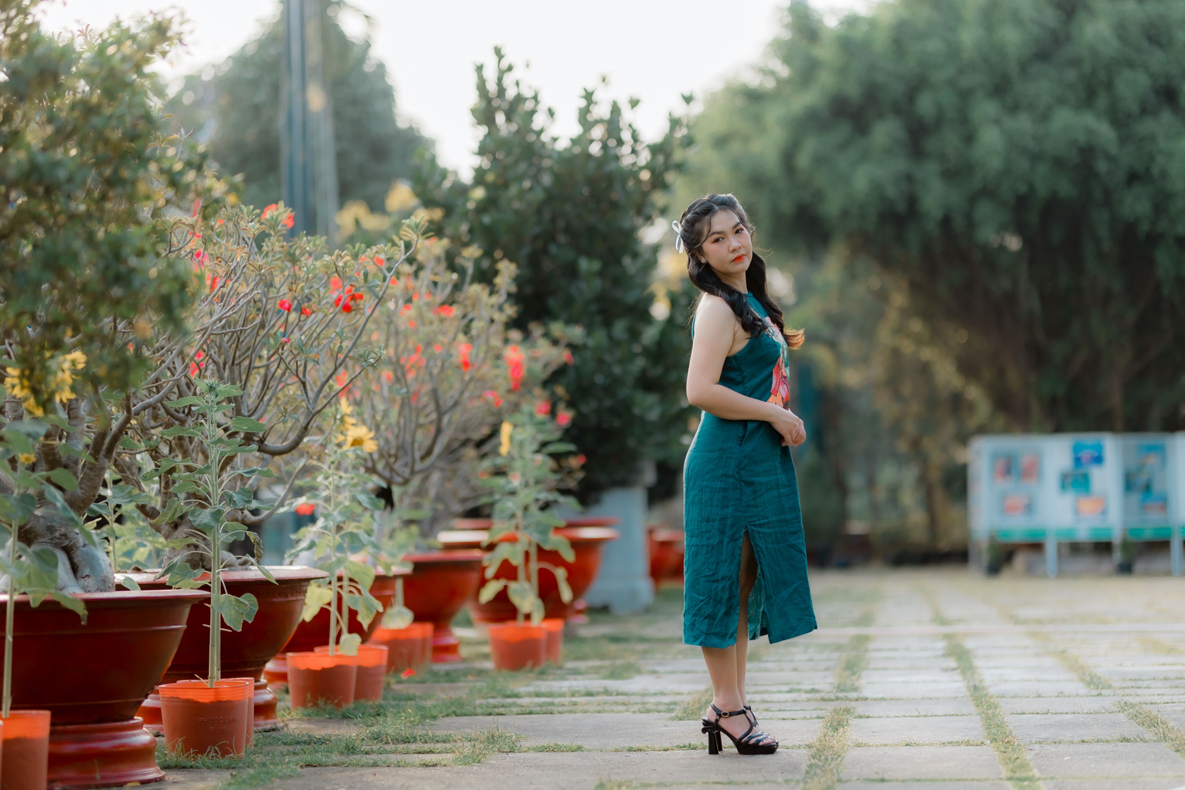 Charming young woman in green dress poses in a serene garden with vibrant flowers and lush greenery.